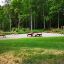 Legepladsen Stænger II med træbro, rutsjebane og picnicborde i en skovklædt park