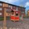 Farverigt legehus 'Verandahuset' på en sandet legeplads foran rødstensbygninger.