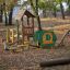 Børnelegehuset 'Alice’s legehus i træ' placeret i en efterårspark med rutsjebaner og klatrestativer.