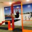 Mand udfører pull-ups på innovativt orangerødt fitnessredskab, Ribbon Fitness II, i moderne bymiljø.
