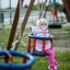 Lille pige nyder en tur på et Gyngestativ til 2 sæder til småbørn på legepladsen.