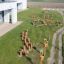 Aerial view of Cape Code wooden playground equipment installed on grass near modern building.