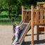 Pige klatrer op ad rutsjebanen på 'Udfordreren Moderne Natur' legetårn i parkmiljø.
