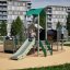 Fæstning med rutsjebane på legeplads med børn, moderne boligområde i baggrunden.