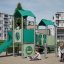 Tårn legehus med rutsjebane på legeplads med børn, grønt legehus med rutsjebane og klatrestativer.