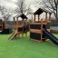 Legehus med rutsjebane, sandkasse og klatrevæg i parkmiljø.