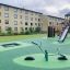 Vippe i stål på legeplads med sikkerhedsgulv og grønne områder.