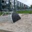 Klatrestativ i stål med klatrevæg og rebstige placeret i en sandkasse.