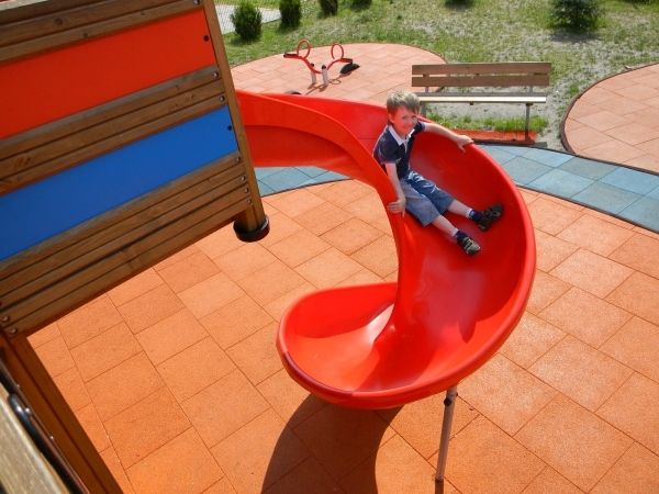Dreng glider ned ad rød rutsjebane på legeplads med Gummifliser 90.