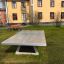 Fristående bordtennisbord i beton placeret på græsset foran en bygning.