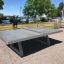 Fristående bordtennisbord af beton placeret i et parkområde nær en sø.