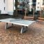 Fristående bordtennisbord i beton placeret udendørs nær bænke og boligbyggeri.