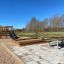 Sandkasse i lærketræ på legeplads med rutsjebane og picnicborde.