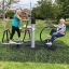 To ældre kvinder motionerer på udendørs fitnessudstyr i en park.