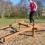 Kvinde træner balance på en træ forhindringsbom i parken.