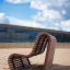 Sofa Wave udendørs bænk (lærk) placeret på en sandstrand med moderne bygning i baggrunden