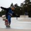 Dreng skateboarder på en beton skatepark med andre børn i baggrunden