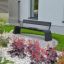 Moderne Sydney udendørs bænk i sort stål, placeret i en have med farverige blomster