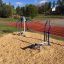Udendørs fitnessudstyr 'Pull Down + Chest Press' i blåt og hvidt på løbebane i solrigt vejr.